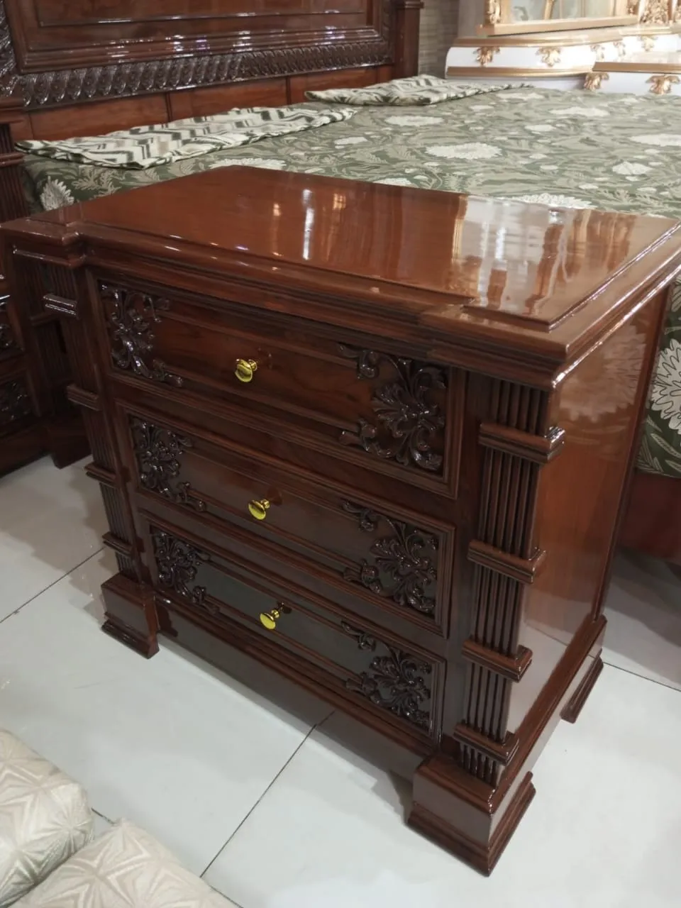 Classic Fluted Chester Sheesham Bedroom Set with 8 Drawer DressingLooking for a solid Sheesham bedroom set with a classic carved look and a proper Chester dressing unit? This crown pediment set is handmade from solid seasoned Sheesham (tali) with a deep walnut high gloss polish that shows the natural grain. The bed has a tall headboard and matching footboard with a smooth centre panel, hand carved floral corners and a wide carved crown top, finished with fluted pillar posts for a traditional master bedroom feel. The suite includes the bed frame, two matching three drawer side tables with carved floral fronts and brass knobs, and a Chester style dressing frame with a large mirror, carved crown top and eight storage drawers in two columns. Every piece uses the same wood, stain and carving style, so the room looks complete without mixing different designs. Made at Alfalah Furniture on Kurri Road, Rawalpindi, with zero MDF and zero lasani board. Custom bed sizes and wood stains are available on request. We deliver across Rawalpindi, Islamabad and nationwide. Message us on WhatsApp for today's price and ready stock timing. — Beds | Alfalah Furniture Rawalpindi